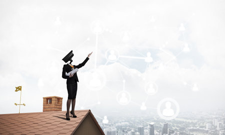 Faceless businesswoman with camera zoom instead of head standing on house roofの写真素材