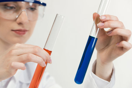 Clinic laboratory analysis and testing. Young woman in protective goggles holding test tube with color liquid. Laboratory assistant comparing samples in test tubes. Biochemistry or chemical research.の写真素材