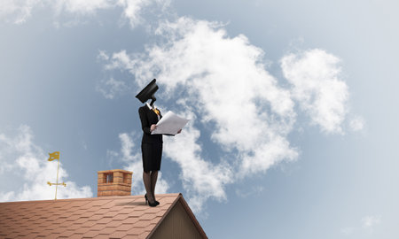 Faceless businesswoman with camera zoom instead of head standing on house roofの写真素材