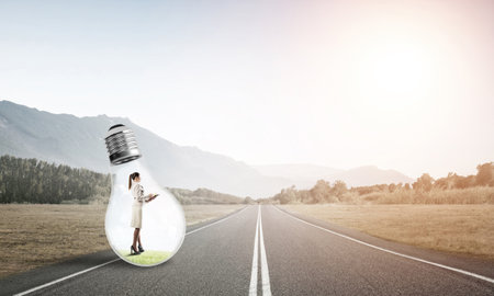 Young businesswoman trapped inside of light bulb on asphalt roadの写真素材