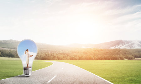 Young businesswoman trapped inside of light bulb on countryside roadの写真素材