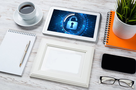 Business workplace with office stuff and tablet with padlock icons on screenの写真素材