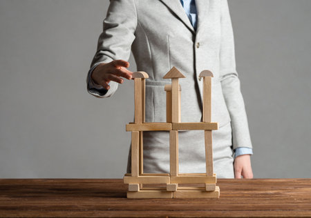 Business woman building tower on table from wooden blocks. Strategy planning and development concept. Young woman wearing formal wear sitting in office interior. Successful company building and growthの写真素材
