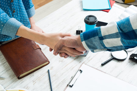 Closeup of male and female hands handshaking after meeting. Creative workspace with color swatches. Interior and textile designing. Coloristics and product branding in studio. Teamwork and creativity.の写真素材