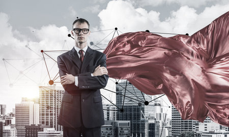 Young confident businessman wearing red cape against modern city backgroundの写真素材