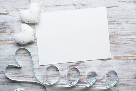 Flat lay composition with white love hearts and ribbon. Blank sheet of white paper on vintage wooden table. Declaration of love letter. Saint Valentines day congratulation. Romantic event invitation.の写真素材