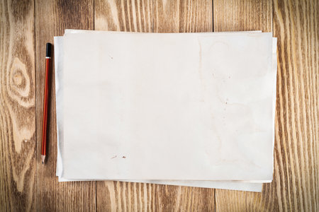 Sheet of paper lying on wooden table. Scrapbooking and hand made creativity. Rectangular blank white paper with pencil. Textured natural wooden background. View from above with copy space.の写真素材