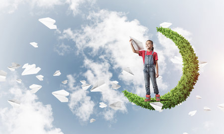 Cute kid girl standing on green moon throwing paper planeの写真素材