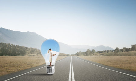 Young businesswoman trapped inside of light bulb on asphalt roadの写真素材