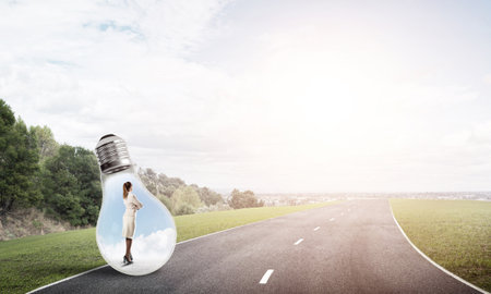 Young businesswoman trapped inside of light bulb on asphalt roadの写真素材