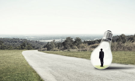Young businessman trapped inside of light bulb on asphalt roadの写真素材