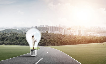 Young businesswoman trapped inside of light bulb on asphalt roadの写真素材