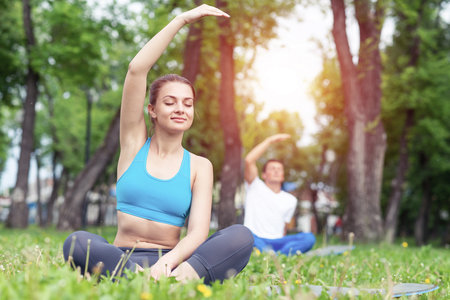 Girl meditates in lotus pose on green grass. Portrait of caucasian young woman with closed eyes. Training and meditation outdoor at summer day. Harmony with nature and relaxation. Practicing of yoga.の写真素材