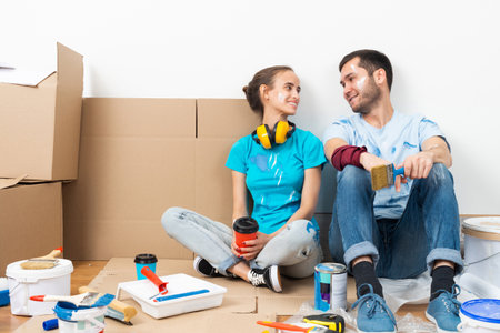 Happy couple together sitting on floor among cardboard boxes. Young man and woman relaxing after moving in their new house. House remodeling and interior renovation. Families moving concept.の写真素材