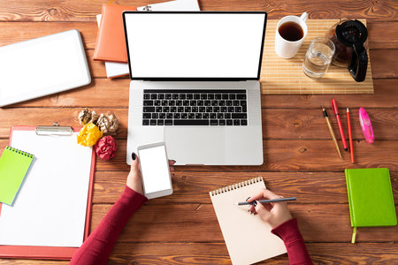 Business woman using smartphone at office desk. Online business app concept. Flat lay office workplace with female hands, laptop and documents. Digital technology and mobile application for business.の写真素材