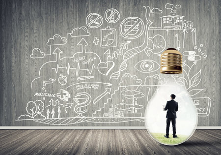 Businessman inside of light bulb in empty concrete room and sketches on wallの写真素材
