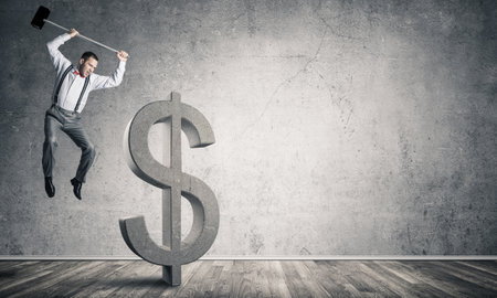 Young furious businessman going to crash with hammer stone dollar symbolの写真素材