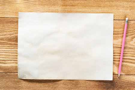 Sheet of paper lying on wooden table. Rectangular blank white old paper with pencil. Textured natural wooden background. Vintage copy space for design. Artist workplace and hand drawn skillsの写真素材