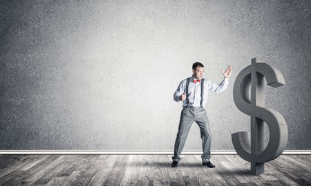 Young furious businessman going to crash with fist stone dollar symbolの写真素材