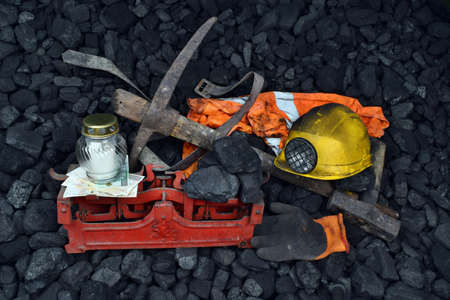 The miner belongings (helmet, gloves, pickaxe, vest, belt), graveyard candle and coal on the weight as concept after the fatal accident in the mineの写真素材