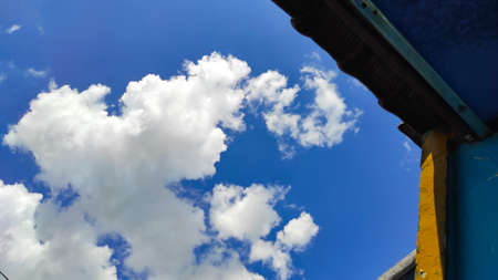 The view of white clouds with a bright blue sky behind the silhouette of the roof of the house in the Cikancung area, Indonesiaの写真素材