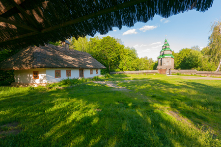 A large old Ukrainian hut on the background of a wooden church in the distanceの写真素材