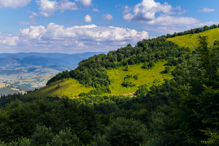 blue sky with clouds over a mountain covered with thick bushes and treesの写真素材