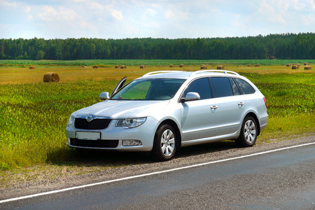 The silver car stopped on the side of the road near a large field with stacks of mown hayの写真素材