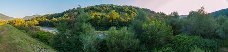 A small fast river against the background of large green hills and mountains with treesの写真素材
