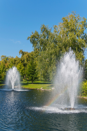 transparent fountains beating from the waters of a pond with green beachesの写真素材