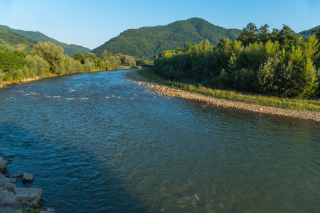Bearing forward its fast water the river. Current between the green coast to the mountain in front of a thick forest.の写真素材