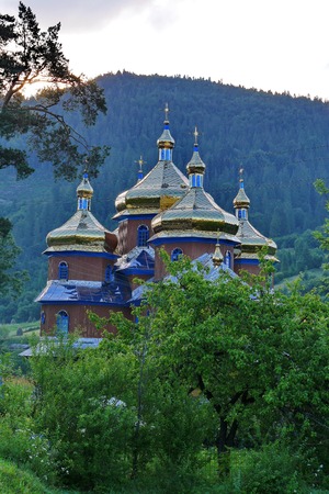 Beautiful church church with large golden domes on the background of huge green mountainsの写真素材