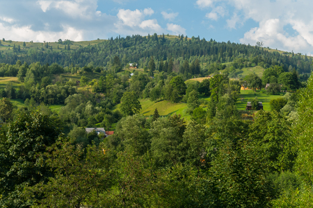 a panorama of green hills and somewhere the roofs of houses looking out among the greeneryの写真素材
