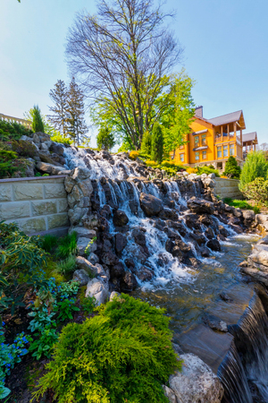 beautiful waterfall on the background of beautiful plants and a country houseの写真素材