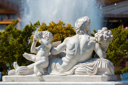 sculpture of plaster in the form of a lying man and boy next to a background of bushes and splashes of a fountainの写真素材