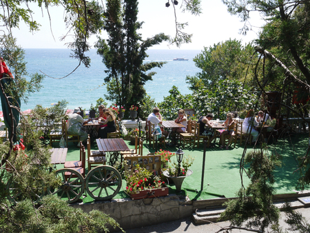 People sitting in a cafe on the embankment near the sea on which the boat sailsのeditorial素材