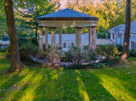A large arbor for rest with columns supporting the roof with benches and a table inside. Located in a park with green grass and beautiful nature.の写真素材