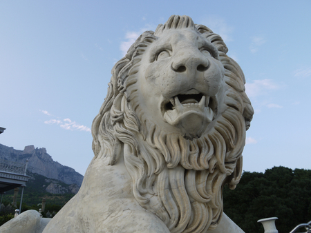 a statue of a grand lion with an open mouth on the background of distant rocks near the palaceの写真素材