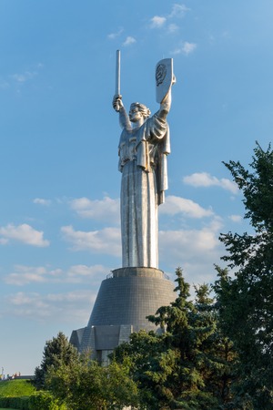 A monument with a high statue of the motherland with arms raised upwards holding a sword in another shield with Soviet symbols standing against the sky with sparse clouds.のeditorial素材