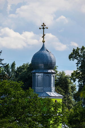 A beautiful view of the glistening dome of the church with a gilded cross standing among the green trees against the background of light transparent clouds in the sky.の写真素材