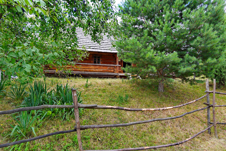 Made of a wooden beam house with a roof standing in the depths of the estate with a stunted vegetation behind a wooden hedge.の写真素材