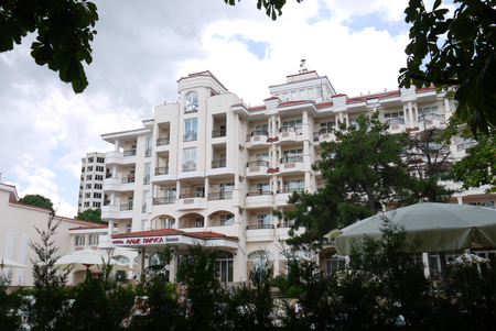 Beautiful views of the beautiful hotel with luxurious architecture and many balconies from under the trees with green foliage growing next to it.のeditorial素材