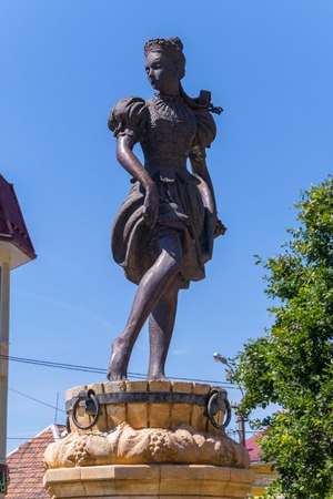 Sculpture of a girl standing on a wooden barrel standing on a pedestal. Against the background of a clear sky without clouds and foliage of trees.のeditorial素材