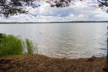 A beautiful view from the shore of a large lake strewn with pine cones on mountains far awayの写真素材