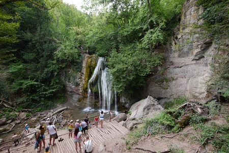 Tourists watch and photograph a beautiful mountain waterfall on a viewing platform near the rocky mountainの写真素材