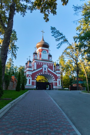 The road leading to the entrance with an arch and domes on the territory of the church parish is located behind the fence. With tall trees growing there.の写真素材