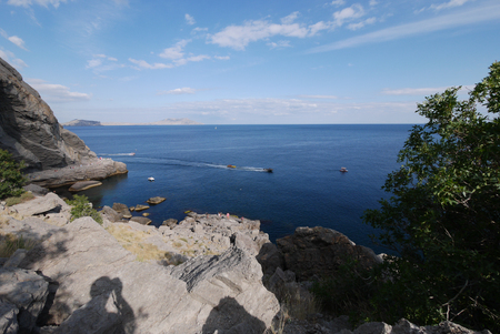 A beautiful sea landscape with stony cliffs with a boat sliding along the surface of the water stretching to the horizon line.の写真素材