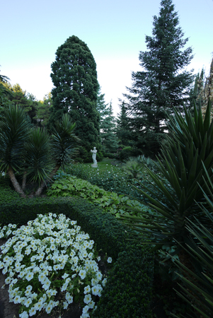 A beautiful white sculpture of gypsum lurking near a green tree next to the lush green flower beds with different vegetationの写真素材