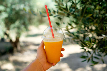 Cool orange ice juice fresh drink holding in a hand on a hot summer sunny dayの写真素材