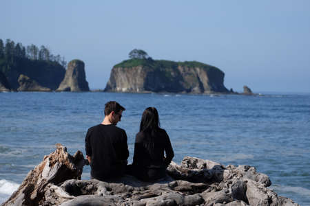 Young couple sitting on a tree log and watching beautiful view of the ocean and an islandの写真素材